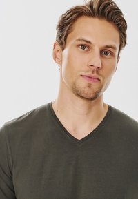 Ciemnozielona koszulka z dekoltem w kształcie litery V, wykonana z miękkiego materiału, z krótkim rękawem i dopasowanym krojem. Prosty design, bez widocznych wzorów czy akcentów.