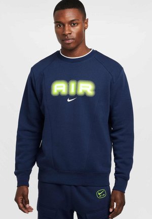 Felpa blu scuro con collo rotondo, caratterizzata da un prominente logo verde "AIR". Texture morbida, polsini e orlo a coste, con dettagli del logo Nike.