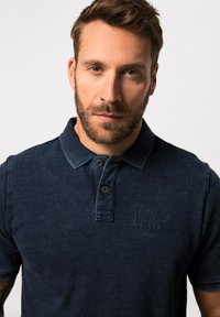 Námořnické polo tričko s texturovanou látkou, klasickým límcem, dvěma knoflíky a vyšitým logem na hrudi. Krátké rukávy, uvolněný střih.