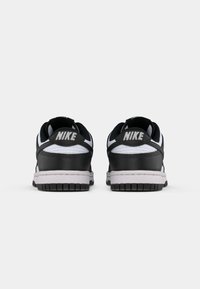 Melnas un baltas Nike sporta kedas ar gludu ādas apdari, noapaļotu siluetu, mīkstu apmalei un baltu gumijas zoli ar teksturētu saķeri.