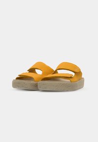 Keltaiset nahkasaappaat, joissa on kaksi leveää nauhaa ja avonainen varvasmuotoilu, joissa on teksturoitu beigekumipohja, jossa on aaltoilumalli.