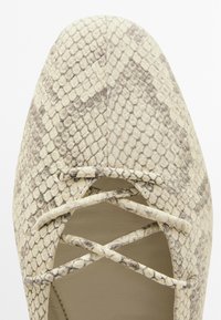 Scarpa con tacco alto stampata in beige con texture a rettile, dotata di lacci incrociati e design a punta.