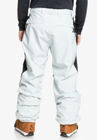 Pantalones de nieve en azul claro con detalles en negro, que presentan un ajuste relajado, cintura elástica y bolsillos con cremallera en los lados.