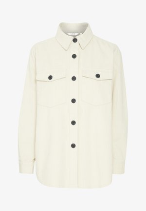 Chemise de couleur crème en velours côtelé doux, avec un devant à boutons, des boutons noirs et deux poches poitrine. Col tailleur et manches longues.