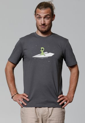 T-shirt en coton gris avec un graphique d'un alien vert sur un avion en papier, sur fond étoilé. Manches courtes.