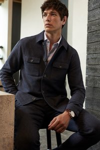 Sötétszürke gyapjú keverék dzseki két mellzsebbel, gombos záródással és galléros nyakkivágással, sötétszürke nadrággal és karórával párosítva.