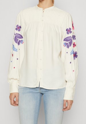 Weiße Bluse mit gefaltetem Vorderteil, hohem Kragen und langen, gepufften Ärmeln, die mit mehrfarbigem Blumenstickerei an den Armen verziert sind.