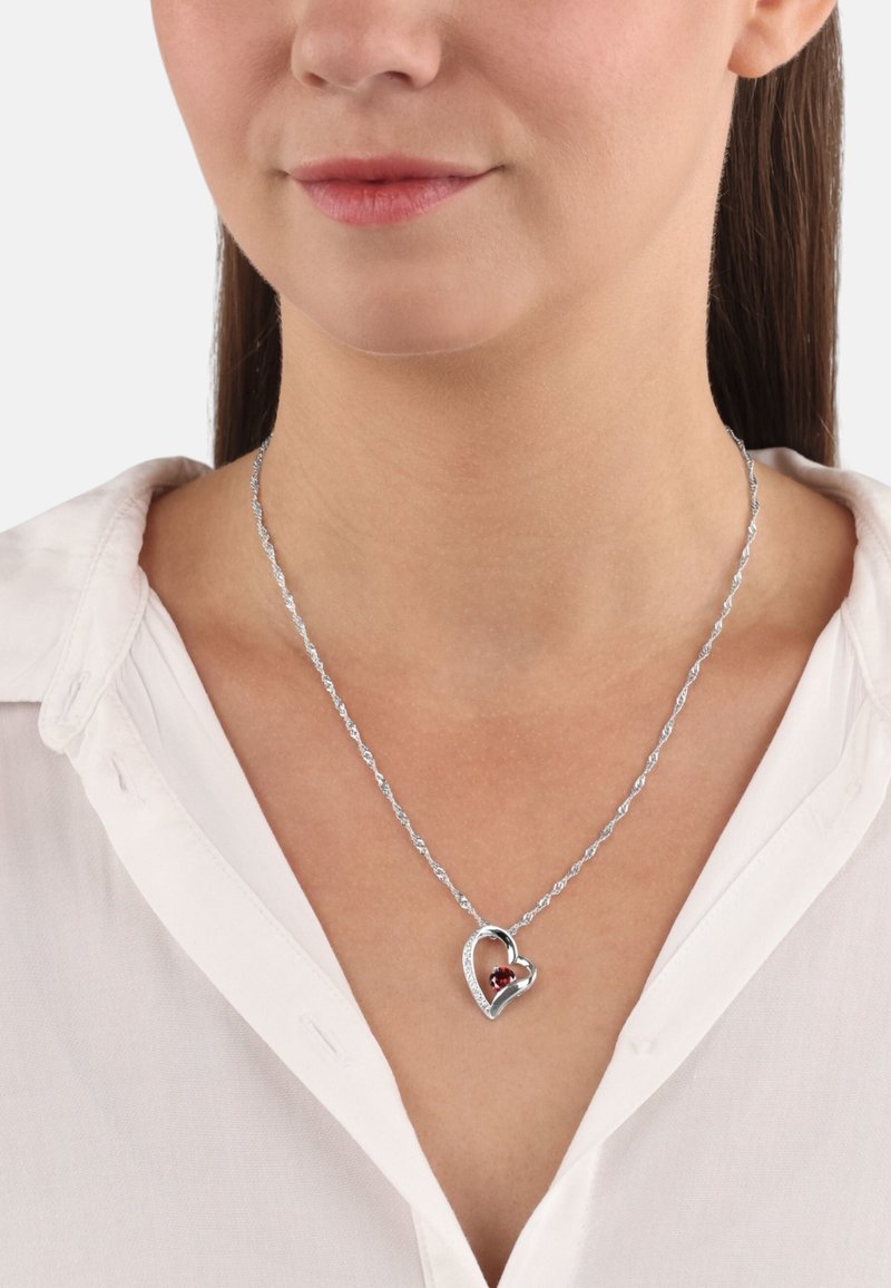 Collar de cadena trenzada en tono plateado que presenta un colgante en forma de corazón con una piedra preciosa transparente y un orbe rojo en el centro.