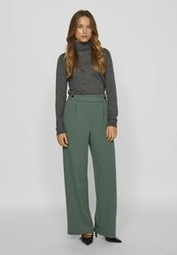 Zelene široke hlače z visokim pasom, plitvicami in gumbi, v kombinaciji s fitted sivo dolgem rokavom turtleneck topom.