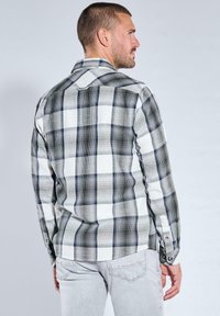 Kariertes Hemd mit einem Muster in Schwarz, Weiß und Grau; Knopfmanschetten; klassischem Kragen; und geradem Rücken.