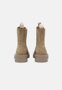 Helle Wildleder-Stiefeletten mit runder Zehenpartie, chunky beigem Absatz und weißen Nähdetails. Mit einer Zuglasche für einfaches Anziehen.