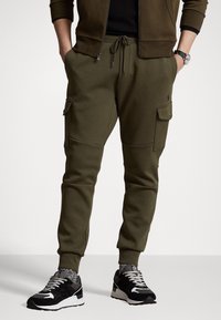 Olive green cargo joggers in a soft material, featuring side pockets and a drawstring waist. Worn with black and gray sneakers, patterned socks.