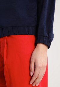 Mörkblå blus med en mjuk, strukturerad finish och samlade manschetter, i kombination med klarröda byxor med en sidoficka.