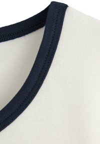 Marineblauwe ribbelkraag op een crèmekleurige stof, die een soepele textuur en een nette naaddetail laat zien. De stof lijkt zacht en duurzaam te zijn.