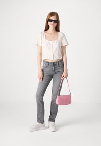 Izgriezts balts kokvilnas blūze ar pogām, pelēkas džinsu bikses, baltas platformas kedas un maza rozā soma. Melni saulesbrilles akcentē apģērbu.