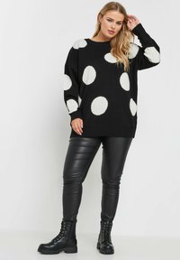 Svart tröja med stora vita prickar, stickad struktur, avslappnad passform och ribbade muddar. Matchad med svarta läderbyxor och kängor.