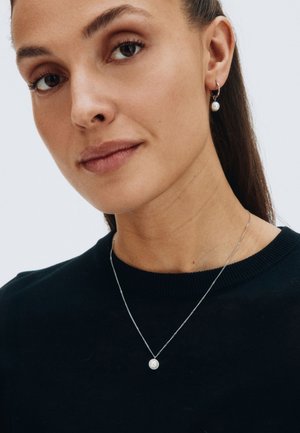 Silver jewelry featuring a simple pearl pendant necklace and matching hoop earrings, worn with a black sweater.