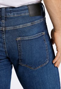 Dunkelblaue Jeans aus Denim mit einer Gesäßtasche mit gelber Ziernaht und einem Leder-Label am Bund. Klassische Passform.