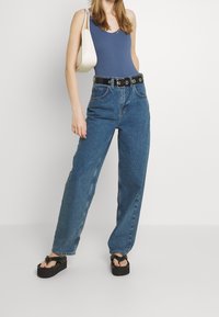 Niebieski prążkowany top na ramiączkach, jasnoniebieskie dżinsy z wysokim stanem z czarnym paskiem z okrągłym zapięciem oraz czarne platformowe klapki.