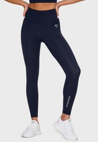 Marina högmidjade leggings tillverkade av stretchigt tyg, prydda med en liten logotyp och ordet "SQUATPROOF" i vitt på vänster ben.