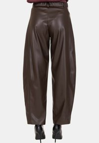 Pantaloni a gamba larga in similpelle marrone scuro con vita elasticizzata arricciata, indossati con scarpe nere con tacco alto, visti da dietro.