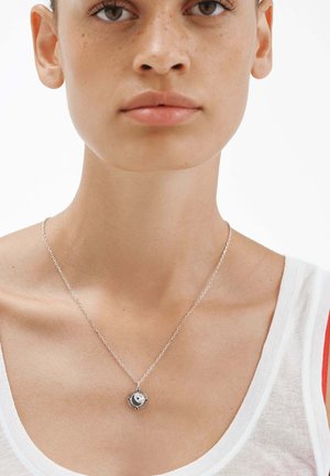 Collar de plata con un colgante redondo, que presenta un diseño central y pequeños acentos azules, suspendido de una delicada cadena.