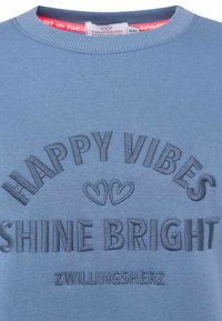 Niebieski sweter z haftowanym napisem "HAPPY VIBES" oraz "SHINE BRIGHT" z podwójnym akcentem serca, wykonany z miękkiego materiału.