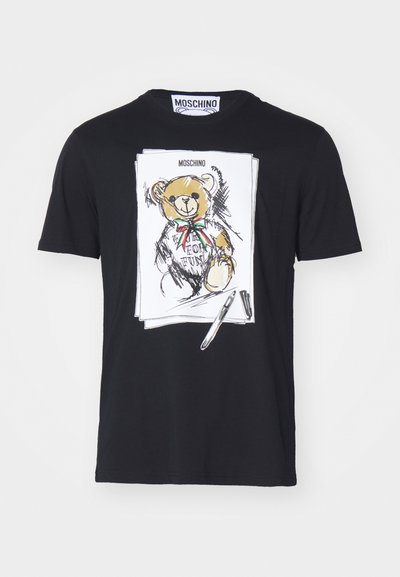 T-shirt en coton noir avec une illustration d'ours blanc, portant un nœud rouge et vert, entourée de détails ressemblant à des croquis et d'un graphique de stylo.