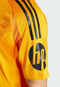 Maglia sportiva gialla con accenti neri, caratterizzata da distintivi modelli grafici e tre strisce nere sulle spalle. Logo HP ben visibile.
