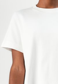 T-shirt en coton blanc avec manches courtes, col rond, texture lisse et sans motifs ni accessoires visibles. Design simple et minimaliste.