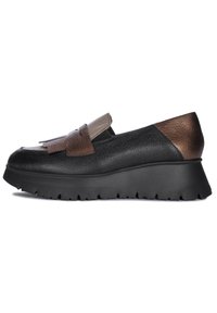 Zapato negro de cuero tipo slip-on con un cuerpo texturizado, acentos en marrón y beige, suela de plataforma con borde dentado y detalles de flecos.