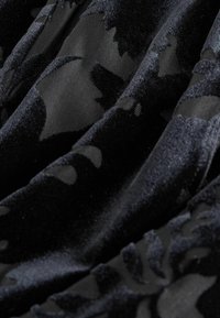 Tineret din catifea neagră cu un model floral texturat, cu textură netedă și moale, având o strălucire variabilă pe suprafață.