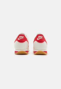 Vörös és fehér Nike sportcipő gumi talppal, sima bőrből készült felső résszel és jellegzetes logóval a hátsó részén.