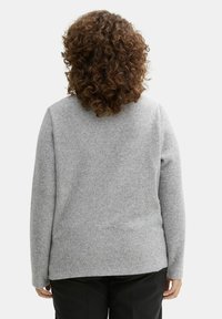 Grå stickad tröja med långa ärmar och rund hals; har en texturerad yta och rakt fåll. Bärs med svarta byxor.