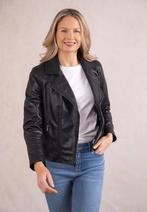 Black leather motorcycle jacket with a notched collar, zippered pockets, and fitted sleeves, worn over a white shirt and blue jeans.
