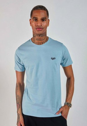T-shirt bleu clair à manches courtes en tissu doux, présentant un petit logo noir brodé sur la poitrine et un col rond classique.