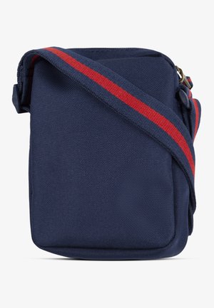 Sac bandoulière en toile bleu marine avec une sangle rayée rouge et bleue, forme carrée, fermeture zippée sur le dessus et détails de couture visibles.