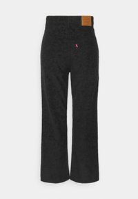 Pantalon large en velours côtelé noir avec un patch de marque en cuir sur la ceinture et une petite étiquette rouge en tissu sur la poche arrière.