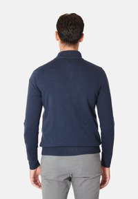 Maglione lavorato a maglia color blu navy con design aderente, maniche lunghe e orlo a coste, abbinato a pantaloni grigi chiari.