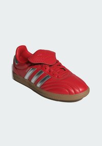 Röd syntetisk sneaker med tre metalliska silverränder, texturerad design på ovandel och en sula av gummigummi. Har en vadderad tunga.
