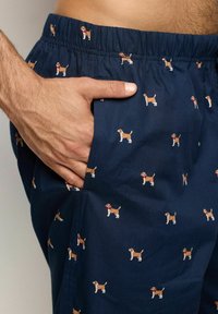 Pantalones cortos de color azul marino con una cintura elástica que presentan un patrón repetido de pequeños perros beagle en estilo de dibujo animado. La tela parece suave.
