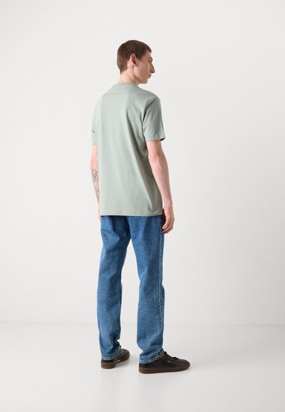 T-shirt en coton vert clair à manches courtes, associé à un jean en denim bleu. L'ensemble présente une coupe décontractée avec une texture lisse.