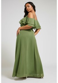 Grön chiffong maxi-klänning med lager av volanger på axlarna, insvängd midja och flytande kjol, med tunna band och en mjuk textur.