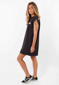 Robe noire à manches courtes avec des accents roses, coupe décontractée et tissu doux. Associée à des baskets noires, mettant en valeur un design décontracté.