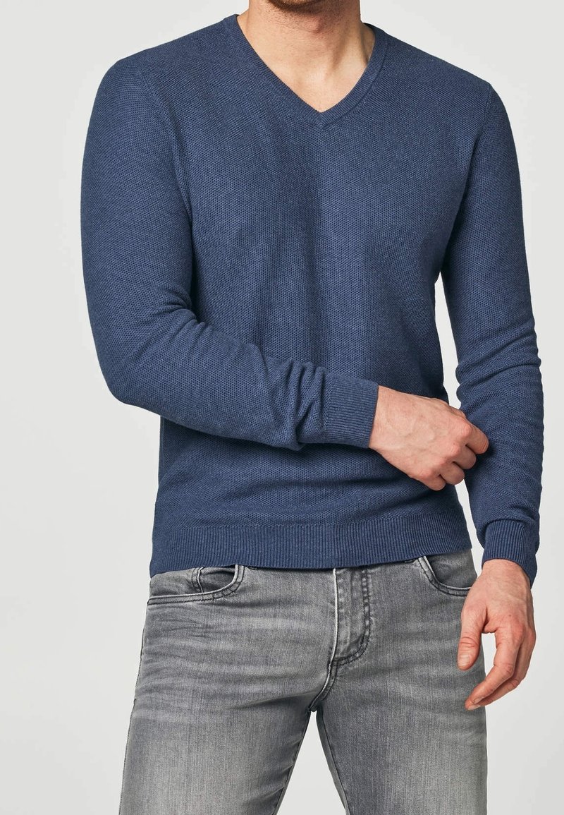 Dunkelblauer V-Ausschnitt, langärmeliger Pullover aus Strick mit gerippten Bündchen und Saum, kombiniert mit grauen Jeans. Strukturmuster im gesamten Pullover.