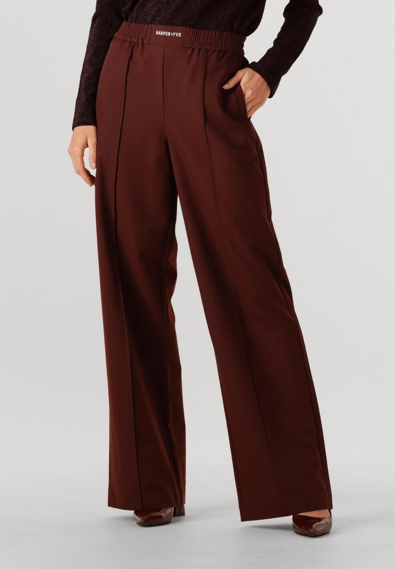 Pantalons larges bordeaux avec une taille élastique et des poches latérales. Tissu lisse avec un tombé subtil et des plis à l'avant pour une forme supplémentaire.