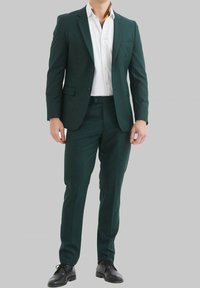 Costume vert en tissu lisse, doté d'un revers cranté, d'une poche poitrine simple et de pantalons slim-fit. Associé à une chemise blanche.