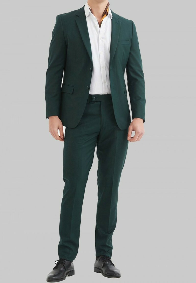 Costume vert en tissu lisse, doté d'un revers cranté, d'une poche poitrine simple et de pantalons slim-fit. Associé à une chemise blanche.