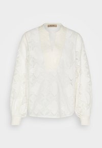 Blouse blanche à manches longues avec motif en dentelle, col en V et poignets froncés, présentée sur un fond uni.
