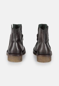Stivaletti alla caviglia in pelle marrone con suola in gomma marrone testurizzata, dotati di chiusura con zip e rivestimento verde. Finitura liscia con dettagli delle cuciture.
